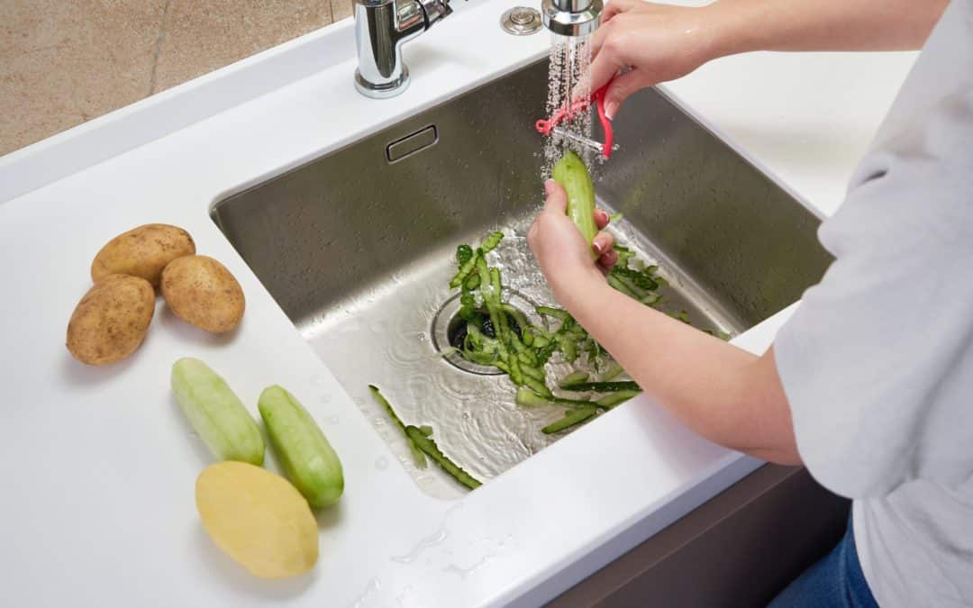 Someone peeling vegetables into kitchen sink.